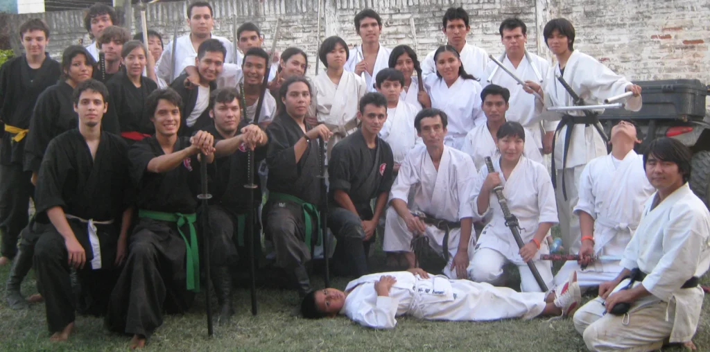 Photo de groupe en plein air : des pratiquants en dōgi noir du Bujinkan et d’autres en dōgi blanc, armes à la main