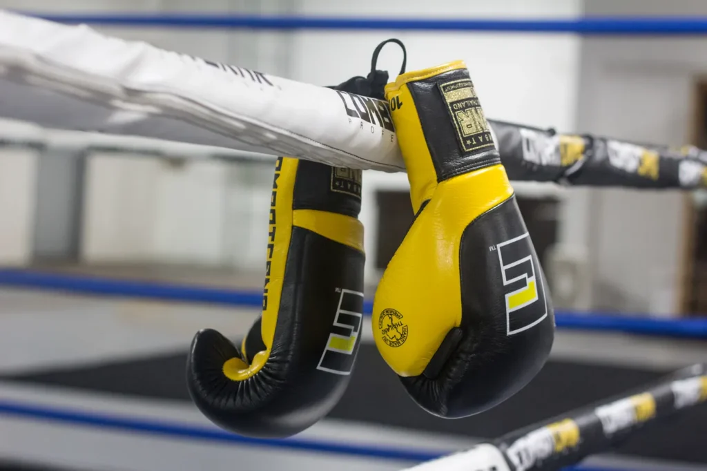 Une paire de gants de boxe noir et jaune suspendue aux cordes d’un ring